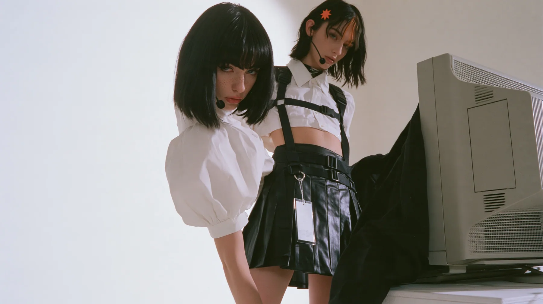 medium shot of a young Caucasian American woman with pale skin and light freckles, a glossy black blunt jaw-length bob with heavy bangs and one clay-orange streak through the bangs, a small flat clay-orange…
