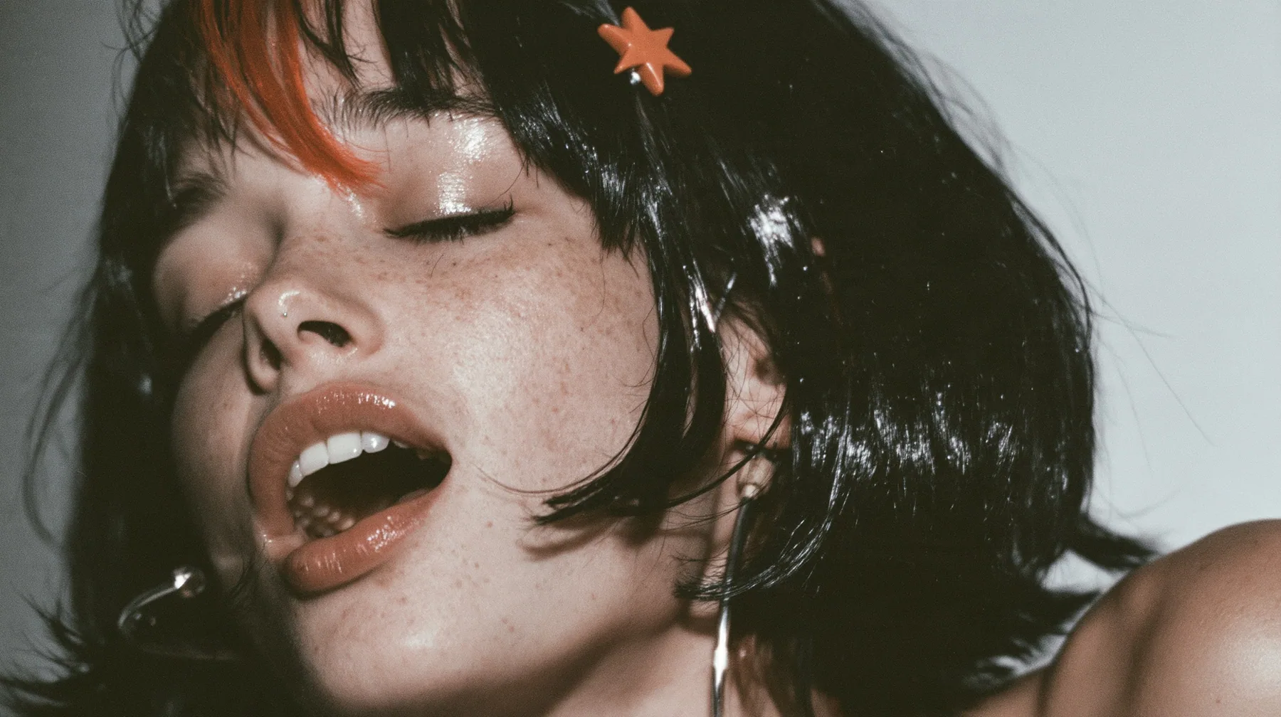 close-up of a young Caucasian American woman with pale skin and light freckles, a glossy black blunt jaw-length bob with heavy bangs and one clay-orange streak through the bangs, a small flat clay-orange…