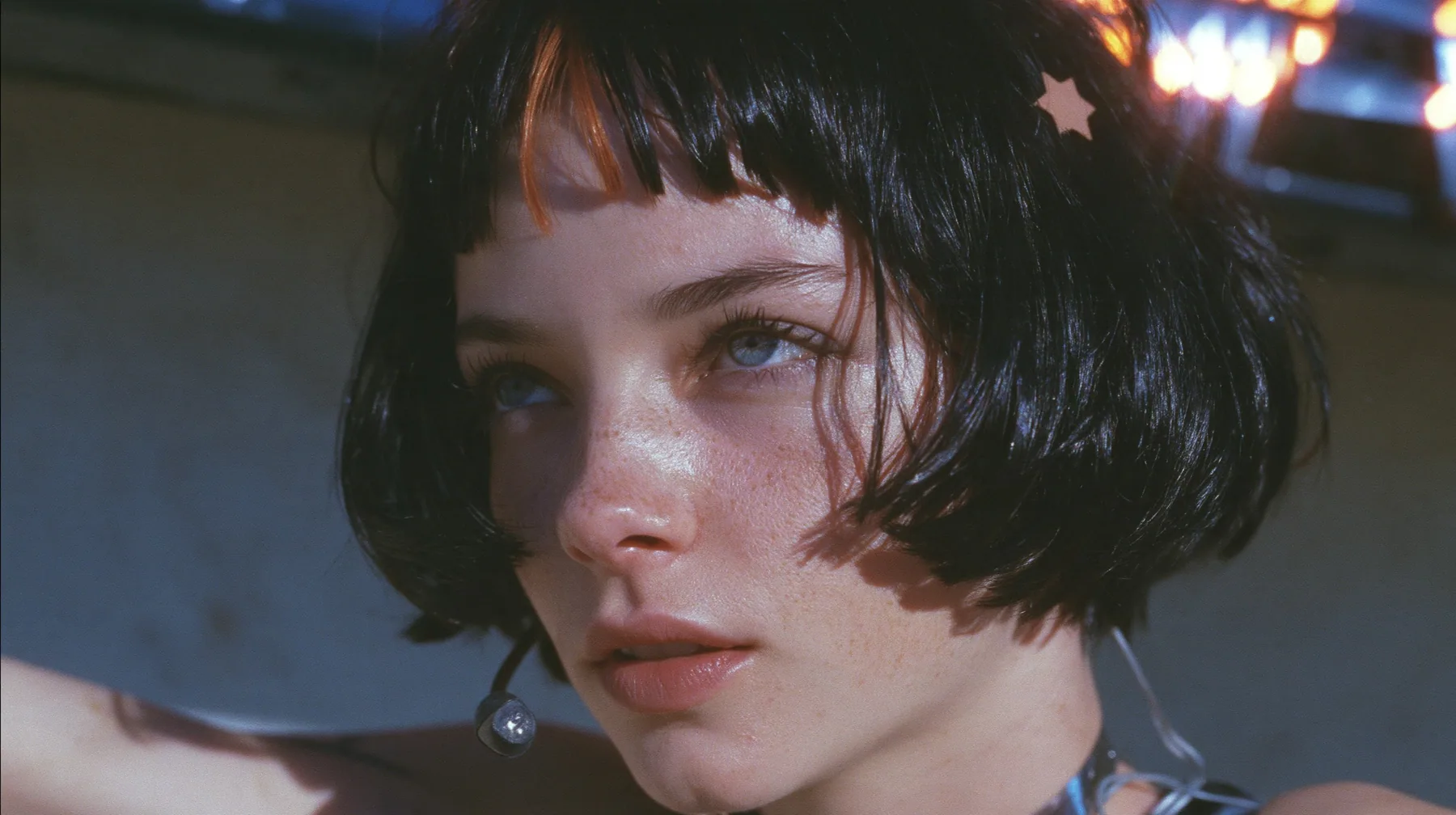 close-up from a low angle of a young Caucasian American woman with pale skin and light freckles, a glossy black blunt jaw-length bob with heavy bangs and one clay-orange streak through the bangs, a small flat…