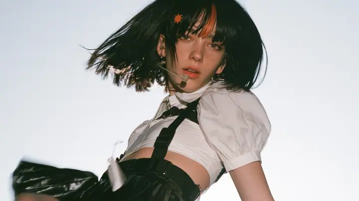 medium shot of a young Caucasian American woman with pale skin and light freckles, a glossy black blunt jaw-length bob with heavy bangs and one clay-orange streak through the bangs, a small flat clay-orange…