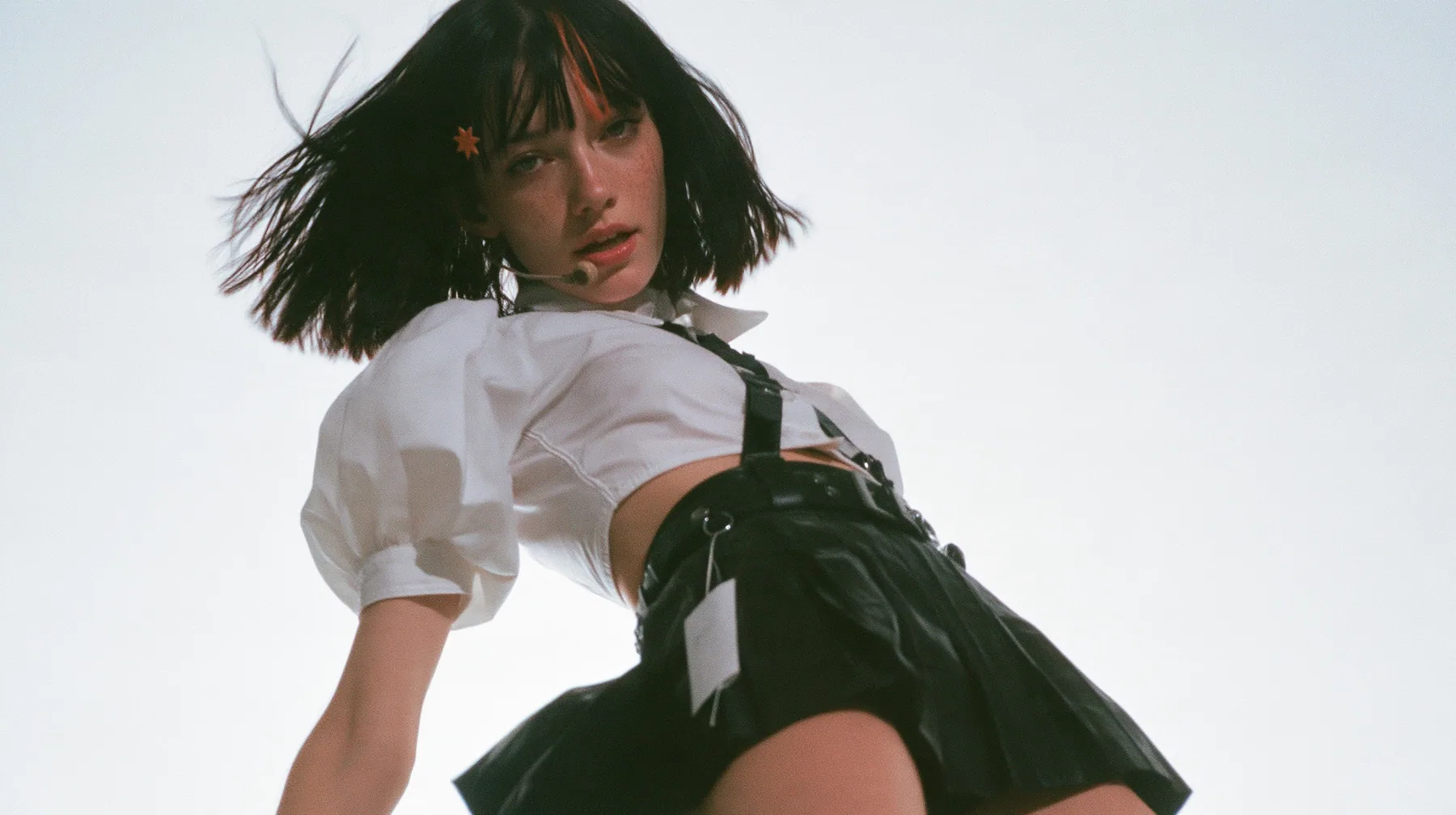medium shot of a young Caucasian American woman with pale skin and light freckles, a glossy black blunt jaw-length bob with heavy bangs and one clay-orange streak through the bangs, a small flat clay-orange…