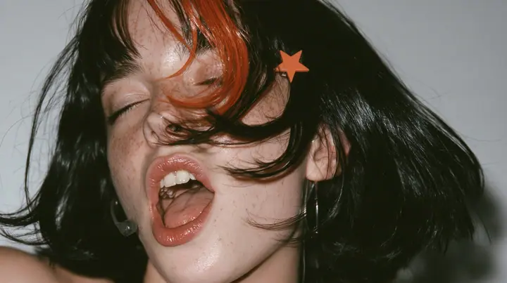 close-up in three-quarter profile of a young Caucasian American woman with pale skin and light freckles, a glossy black blunt jaw-length bob with heavy bangs and one clay-orange streak through the bangs, a small flat…
