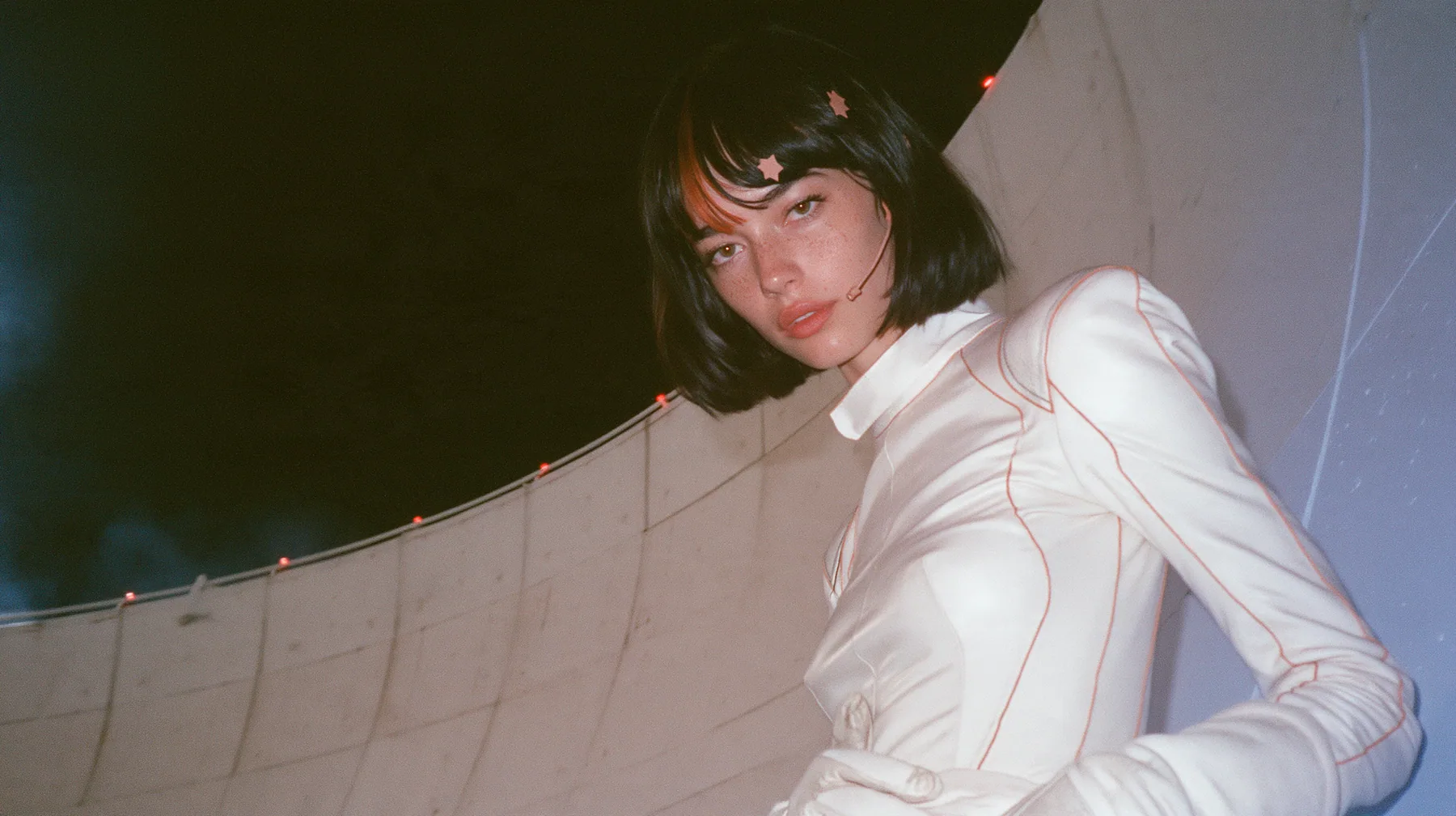medium shot from low, a 28-year-old Caucasian American woman with a grown-up angular face, defined cheekbones and a strong jawline, pale skin and light freckles, a glossy black blunt jaw-length bob with heavy…