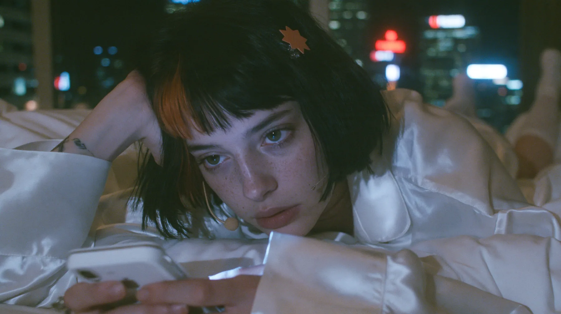medium shot at mattress height, a 28-year-old Caucasian American woman with a grown-up angular face, defined cheekbones and a strong jawline, pale skin and light freckles, a glossy black blunt jaw-length bob with…
