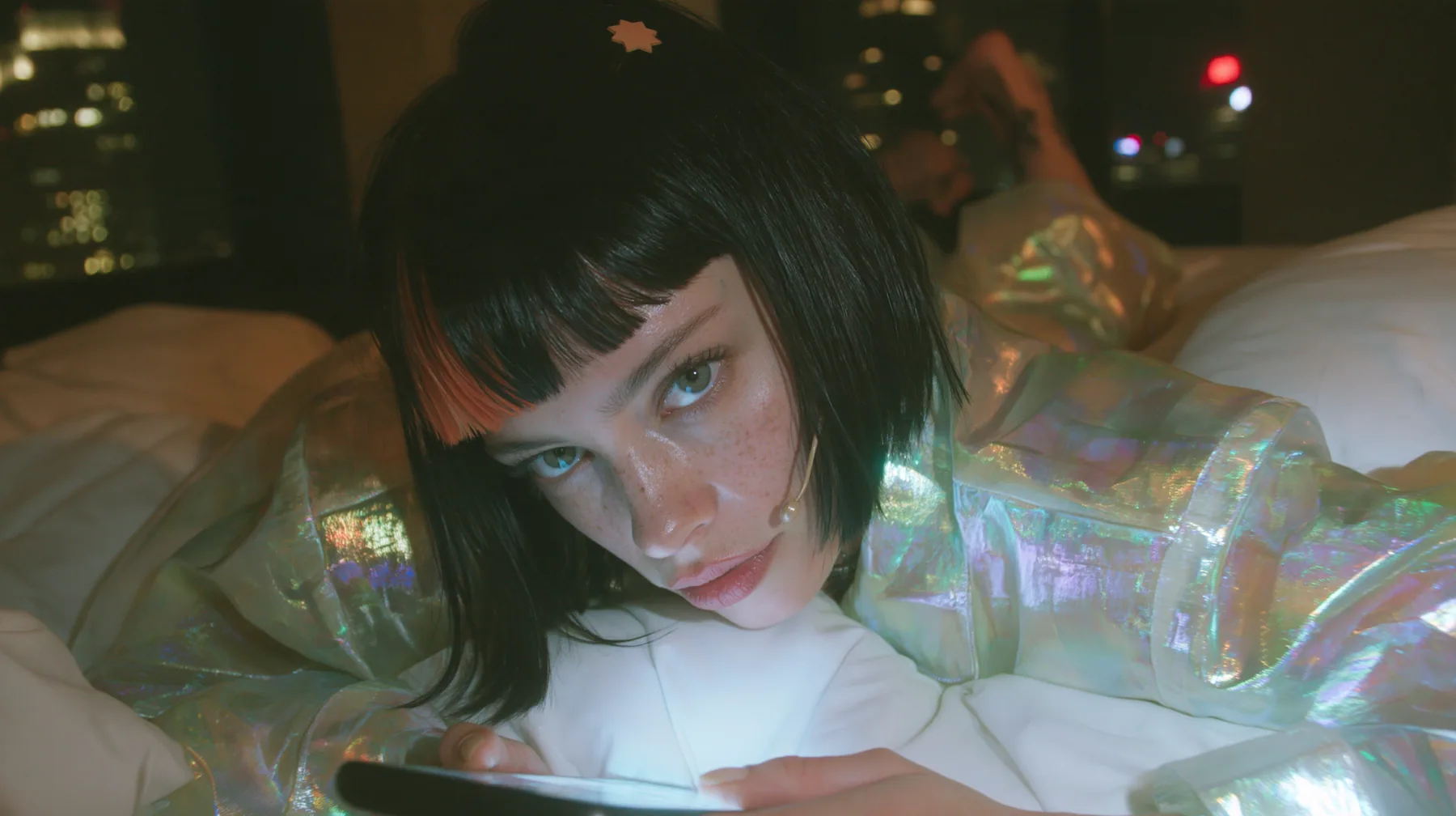 medium shot at mattress height, a 28-year-old Caucasian American woman with a grown-up angular face, defined cheekbones and a strong jawline, pale skin and light freckles, a glossy black blunt jaw-length bob with…