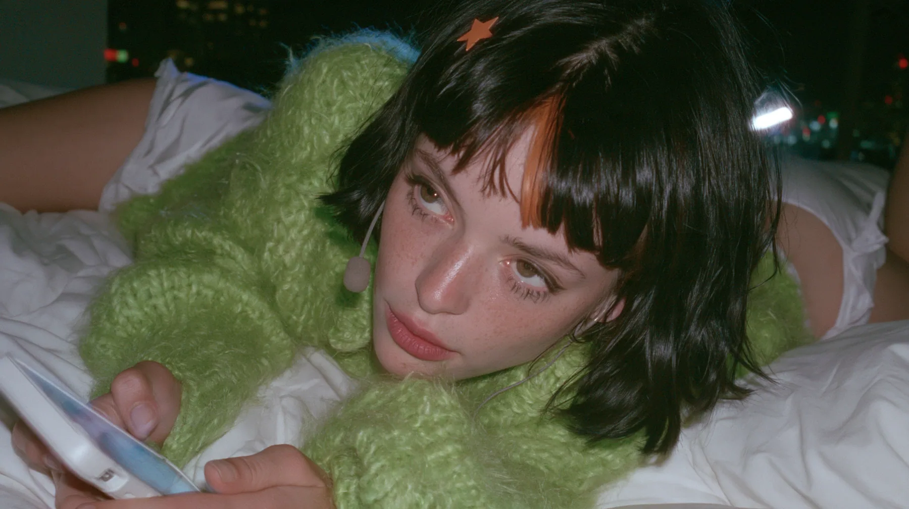 medium shot at mattress height, a 28-year-old Caucasian American woman with a grown-up angular face, defined cheekbones and a strong jawline, pale skin and light freckles, a glossy black blunt jaw-length bob with…