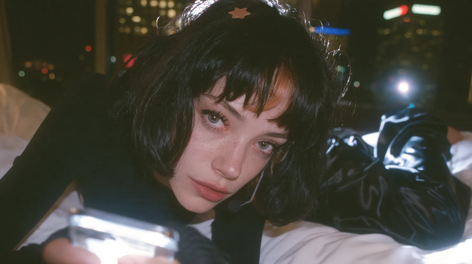 medium shot at mattress height, a 28-year-old Caucasian American woman with a grown-up angular face, defined cheekbones and a strong jawline, pale skin and light freckles, a glossy black blunt jaw-length bob with…