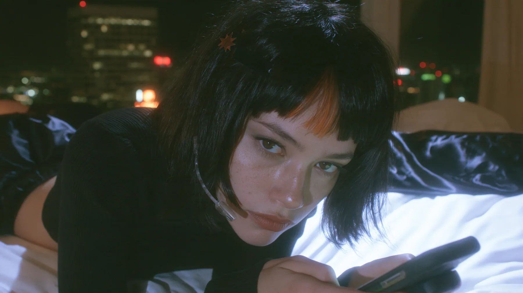 medium shot at mattress height, a 28-year-old Caucasian American woman with a grown-up angular face, defined cheekbones and a strong jawline, pale skin and light freckles, a glossy black blunt jaw-length bob with…