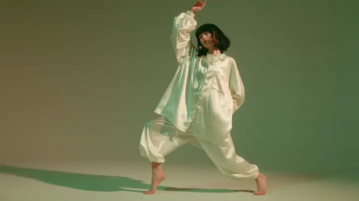 full-length studio photograph, a Caucasian American woman in her late twenties with pale skin and a glossy black blunt bob with heavy straight bangs and one clay-orange streak, a thin headset microphone, in oversized…