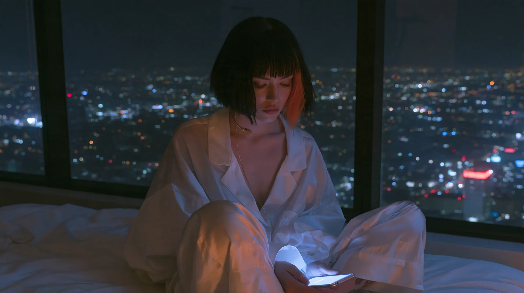 wide shot of a dark minimal high-rise bedroom at night, a floor-to-ceiling window over a glittering city, a Caucasian American woman in her late twenties with pale skin and a glossy black blunt bob with heavy…