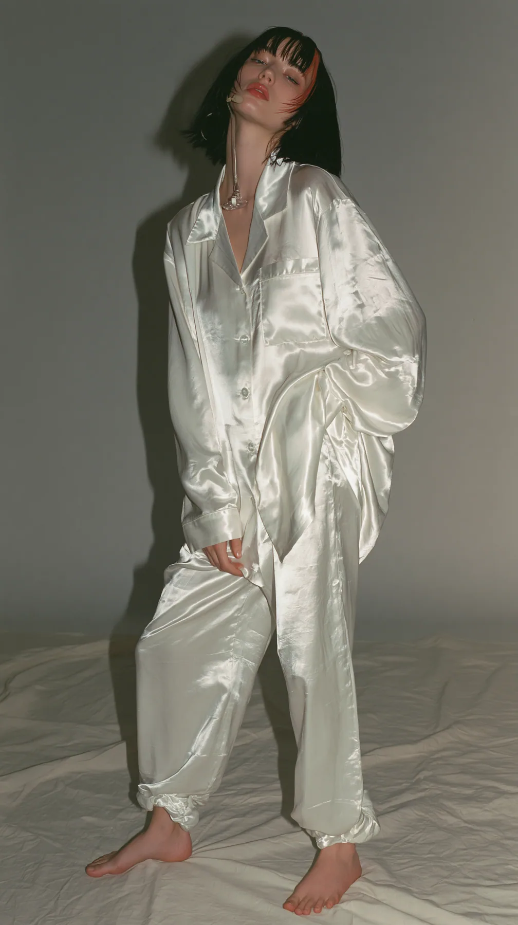 full-length shot, a Caucasian American woman in her late twenties with pale skin and a glossy black blunt bob with heavy straight bangs and one clay-orange streak, a thin headset microphone, in oversized white…
