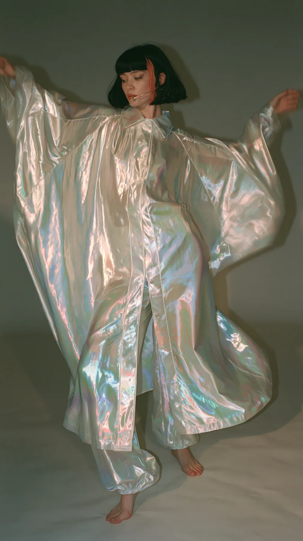 full-length shot, a Caucasian American woman in her late twenties with pale skin and a glossy black blunt bob with heavy straight bangs and one clay-orange streak, a thin headset microphone, in oversized iridescent…