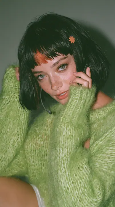 medium-full shot, a 28-year-old Caucasian American woman with a grown-up angular face, defined cheekbones and a strong jawline, pale skin and light freckles, a glossy black blunt jaw-length bob with heavy straight…