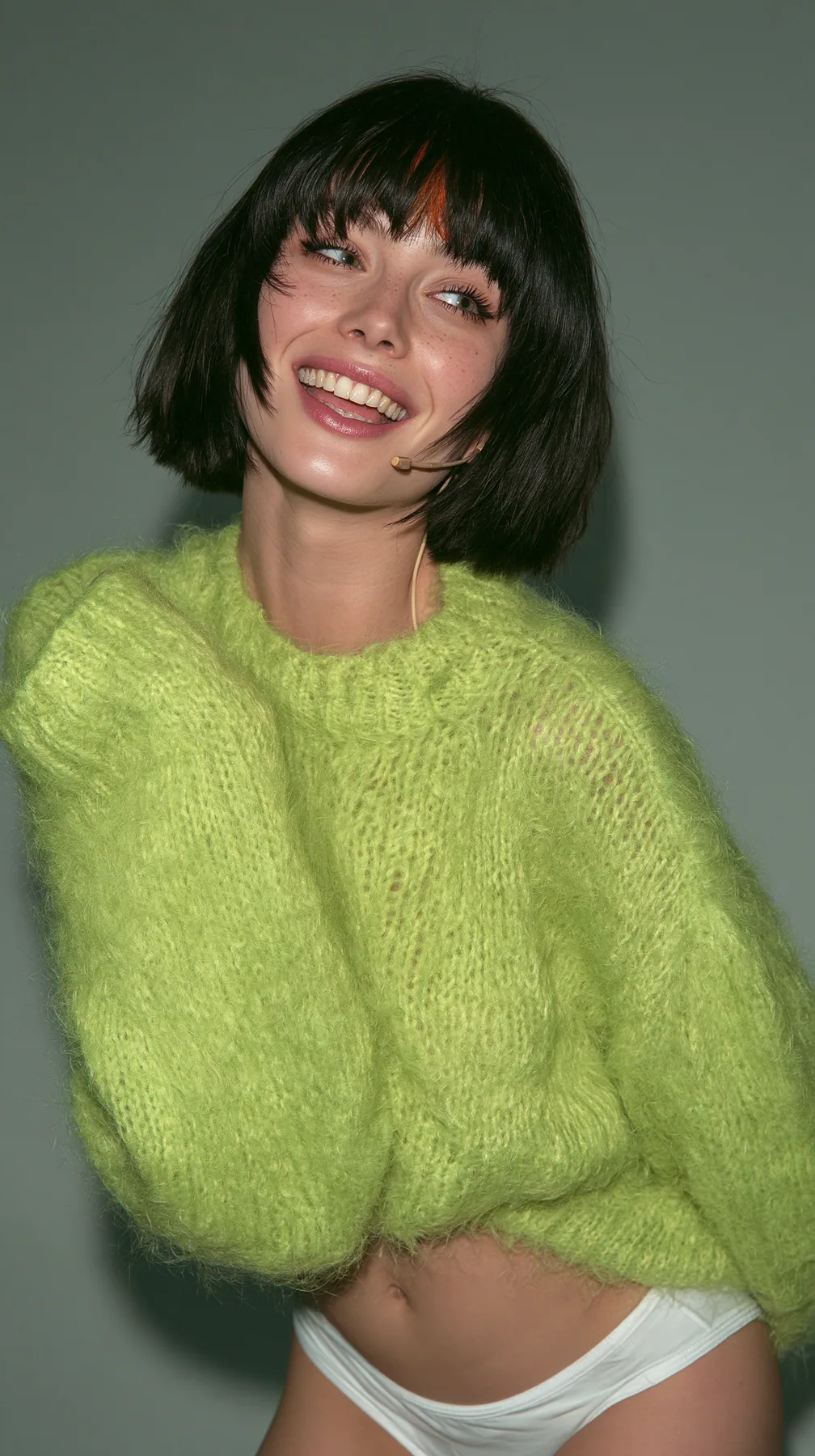 medium-full shot, a 28-year-old Caucasian American woman with a grown-up angular face, defined cheekbones and a strong jawline, pale skin and light freckles, a glossy black blunt jaw-length bob with heavy straight…