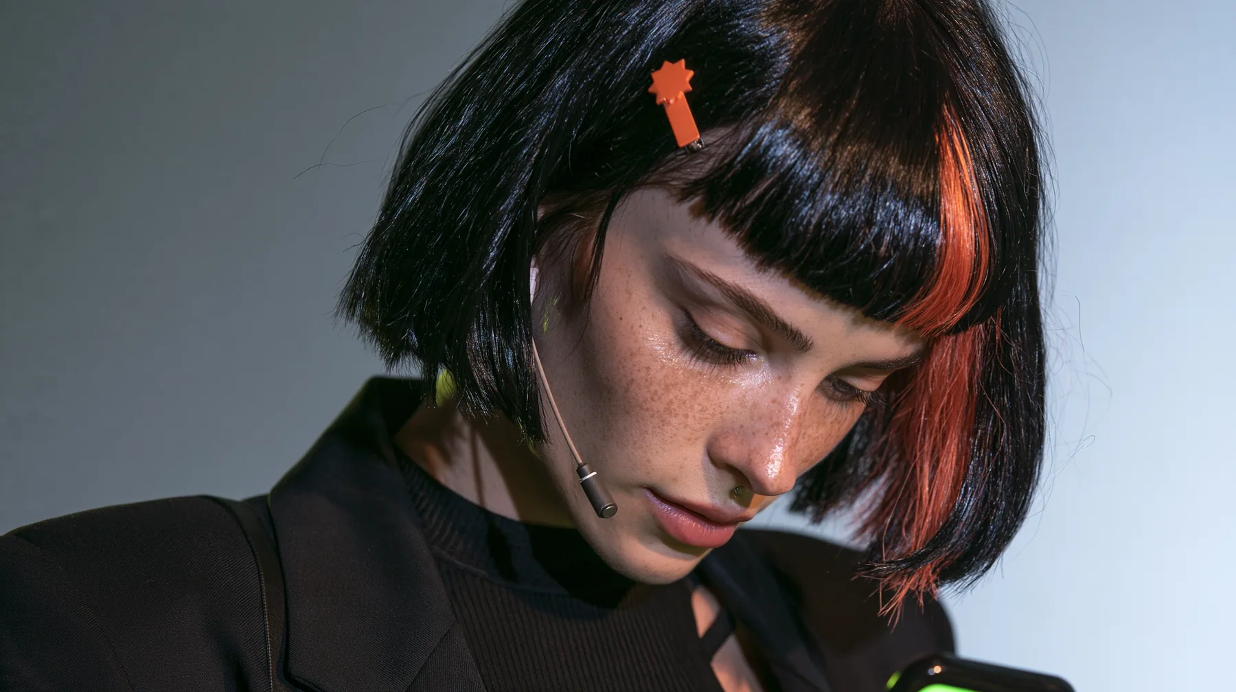 over-the-shoulder medium close-up, a 28-year-old Caucasian American woman with a grown-up angular face, defined cheekbones and a strong jawline, pale skin and light freckles, a glossy black blunt jaw-length bob with…
