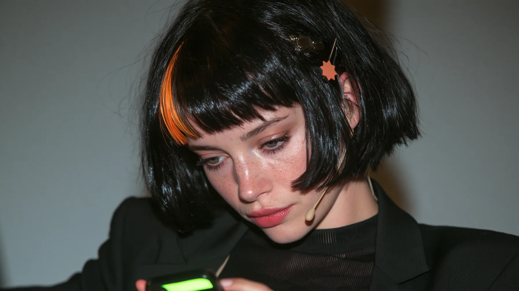 over-the-shoulder medium close-up, a 28-year-old Caucasian American woman with a grown-up angular face, defined cheekbones and a strong jawline, pale skin and light freckles, a glossy black blunt jaw-length bob with…