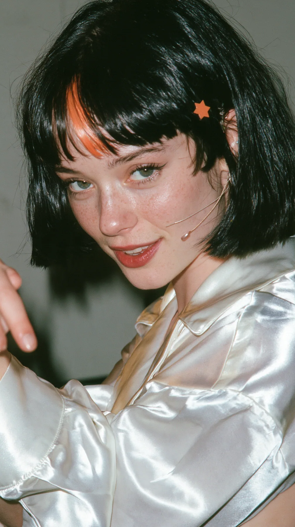 medium-full shot, a 28-year-old Caucasian American woman with a grown-up angular face, defined cheekbones and a strong jawline, pale skin and light freckles, a glossy black blunt jaw-length bob with heavy straight…