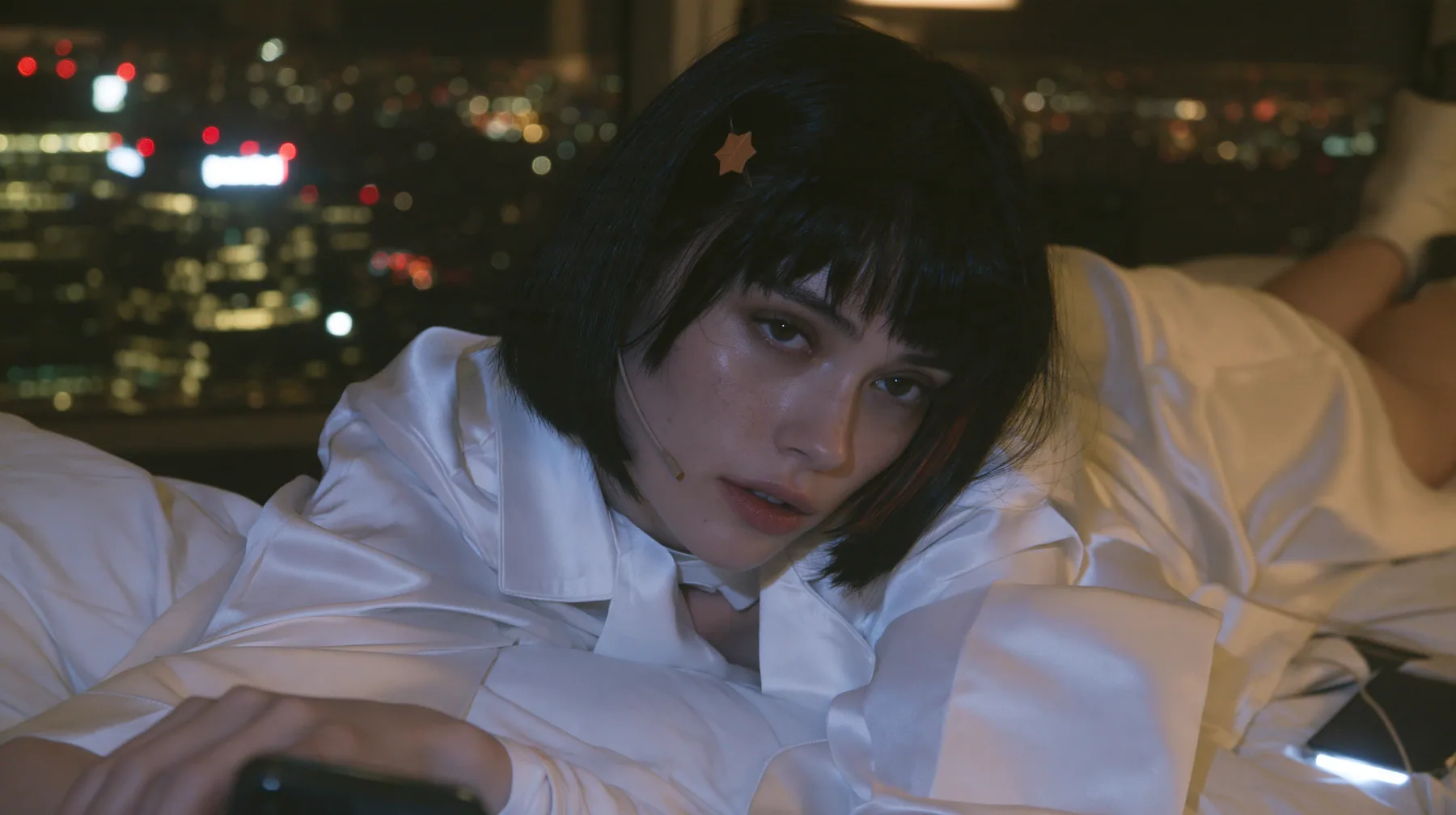 medium shot at mattress height in a dark high-rise bedroom at night, a 28-year-old Caucasian American woman with a grown-up angular face, defined cheekbones and a strong jawline, pale skin and light freckles, a…