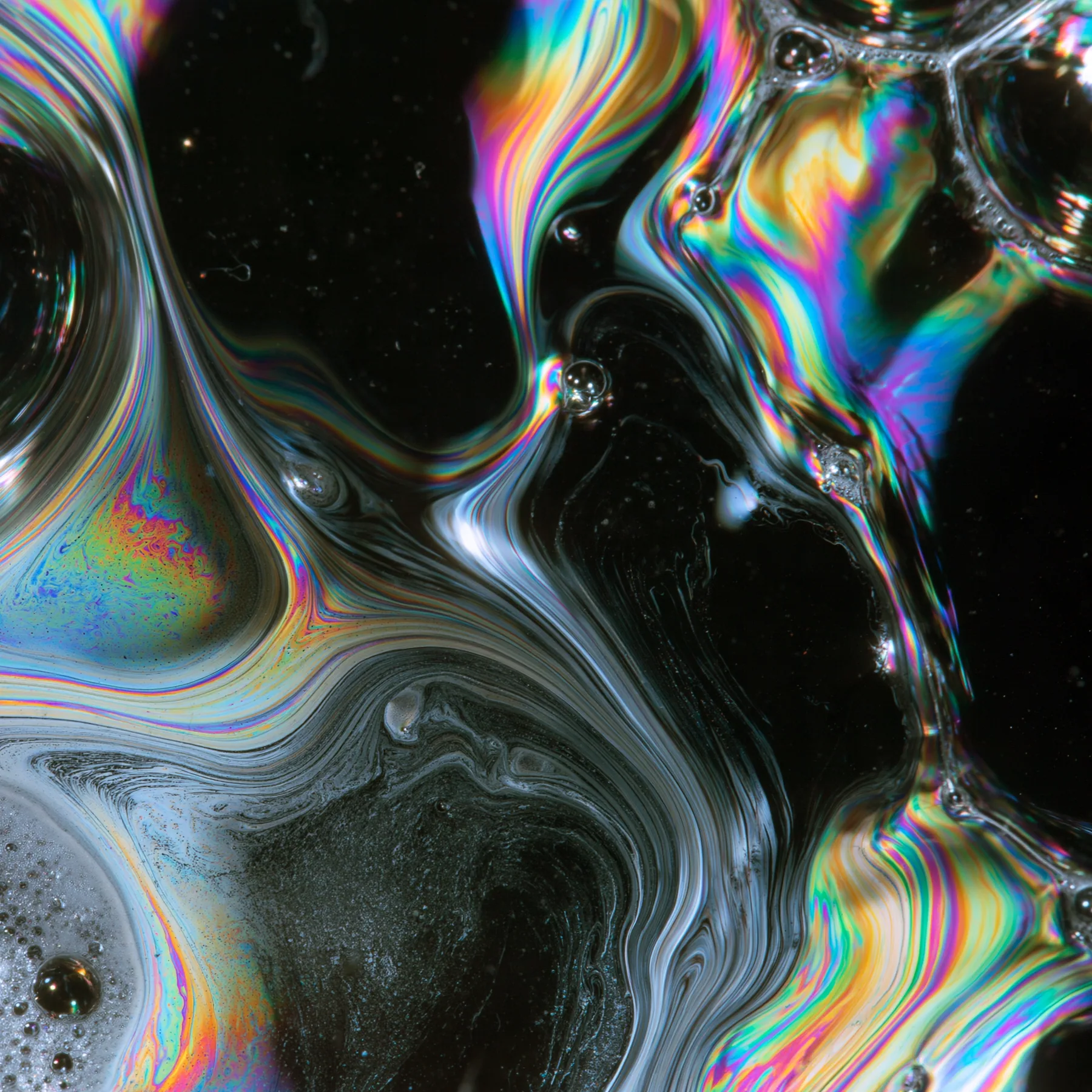 macro of a soap film with swirling iridescent interference colours on black, scientific photograph, no text, no letters, no logos