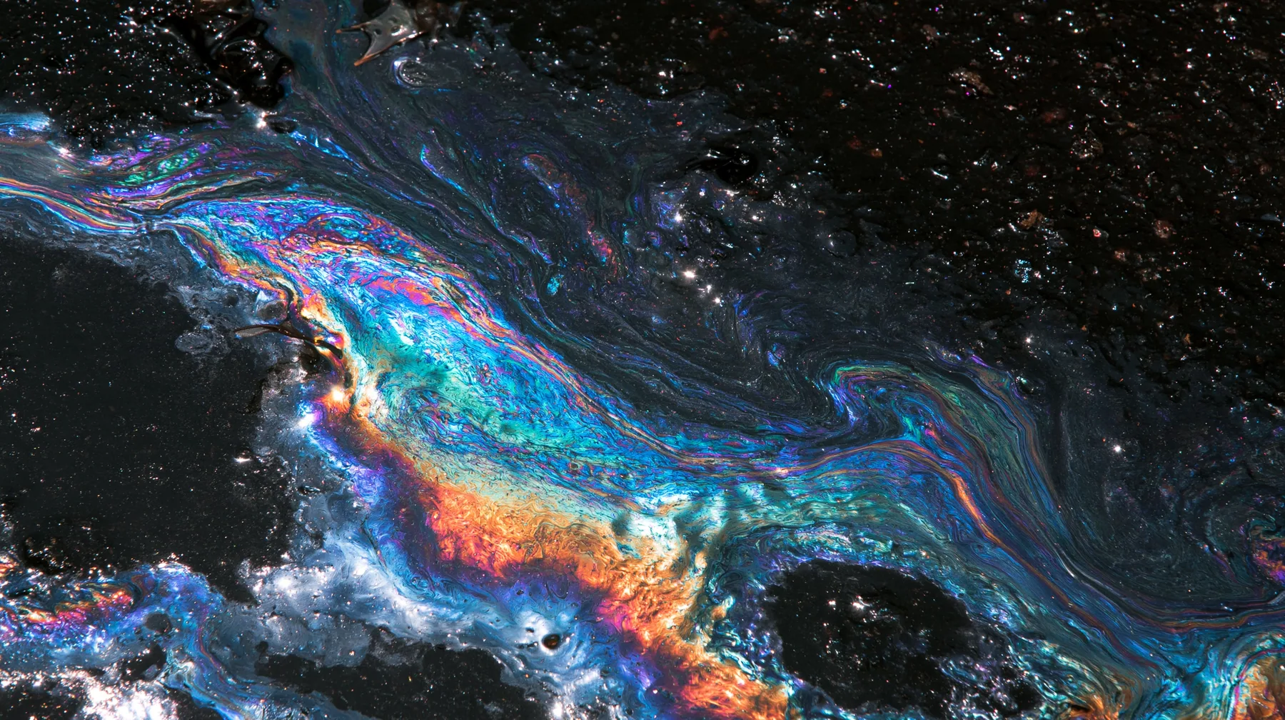 macro of an oil slick rainbow on wet black asphalt at night, iridescent swirls, no text, no letters, no logos