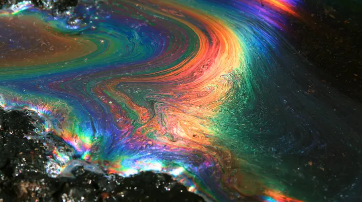 macro of an oil slick rainbow on wet black asphalt at night, iridescent swirls, no text, no letters, no logos