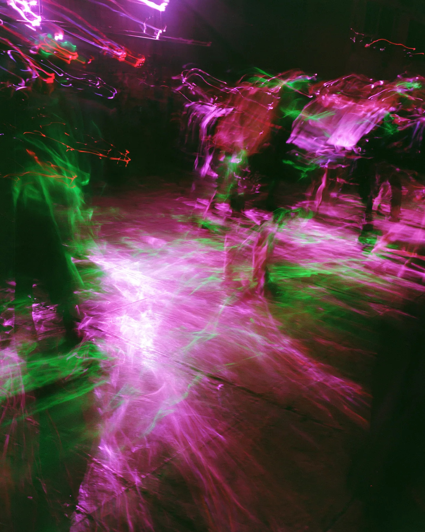 a long-exposure photograph of magenta and acid-green light trails over a dark dance floor, smeared, euphoric, no text, no letters, no logos