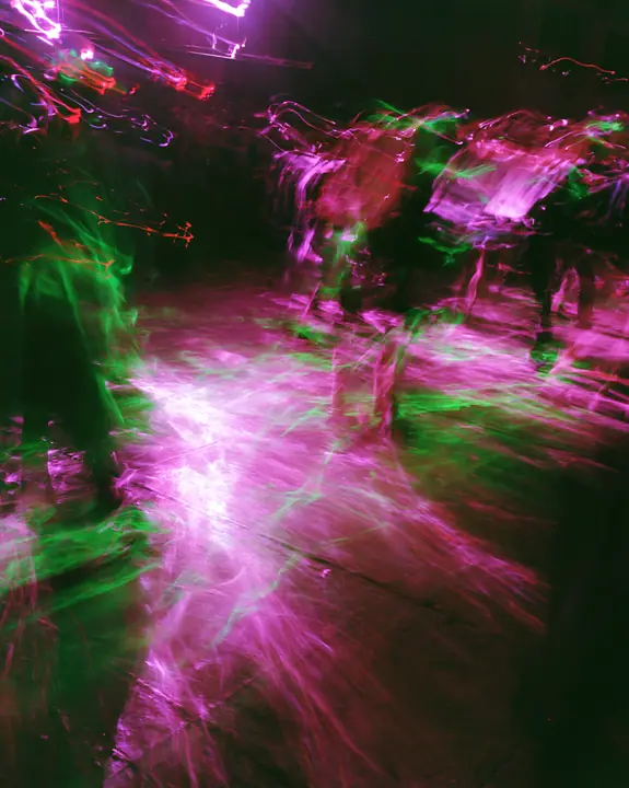 a long-exposure photograph of magenta and acid-green light trails over a dark dance floor, smeared, euphoric, no text, no letters, no logos