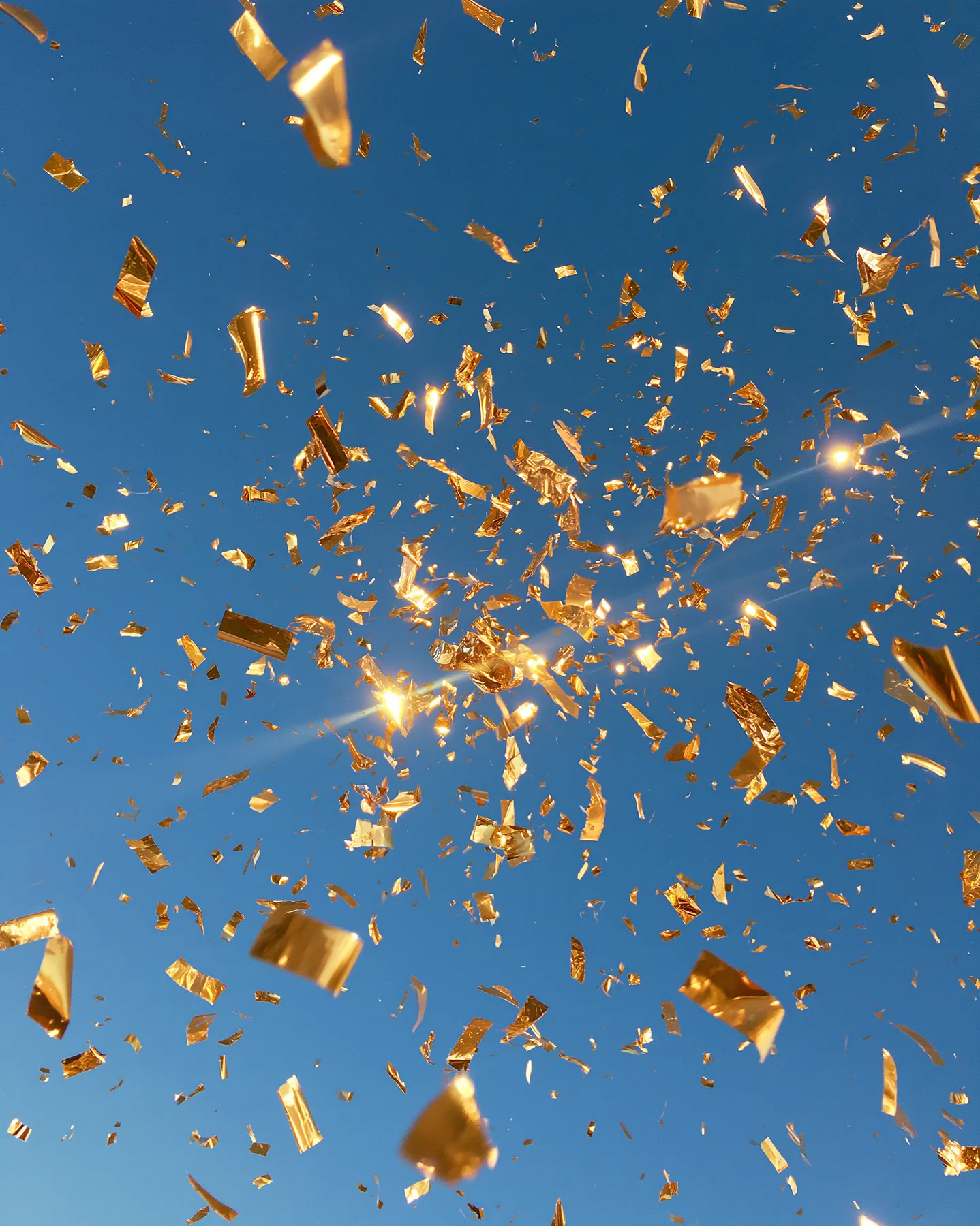 a burst of gold confetti against a clear blue sky, celebration, crisp, no text, no letters, no logos