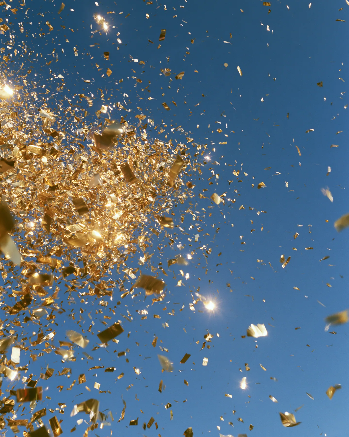 a burst of gold confetti against a clear blue sky, celebration, crisp, no text, no letters, no logos