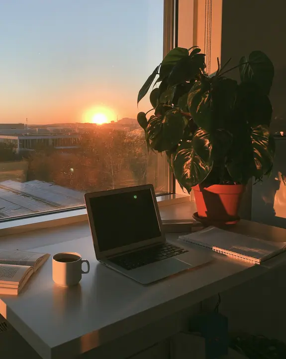 an open laptop on a white desk at sunrise beside a coffee and a plant, clean, aspirational, no text, no letters, no logos