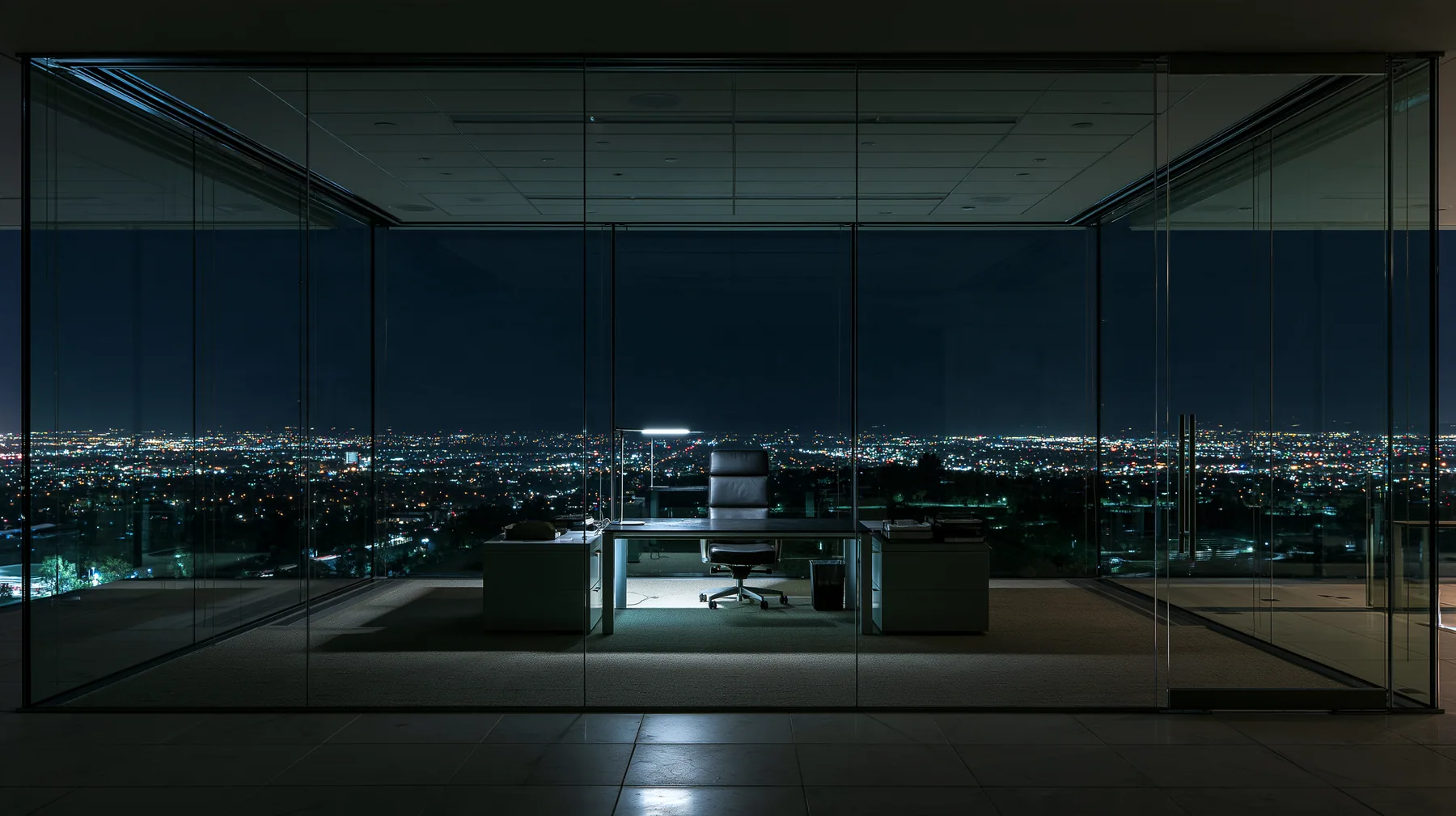 an empty glass-walled office at night, city lights, one lamp left on, wide angle, no text, no letters, no logos