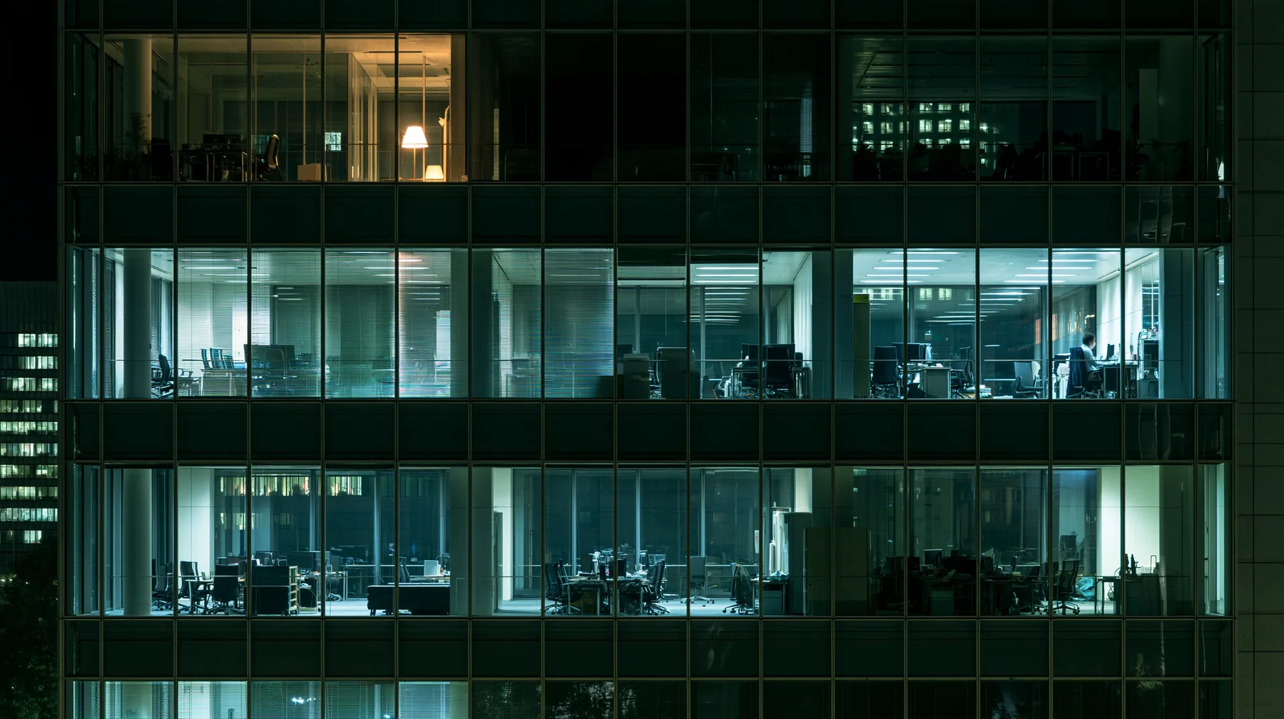 an empty glass-walled office at night, city lights, one lamp left on, wide angle, no text, no letters, no logos
