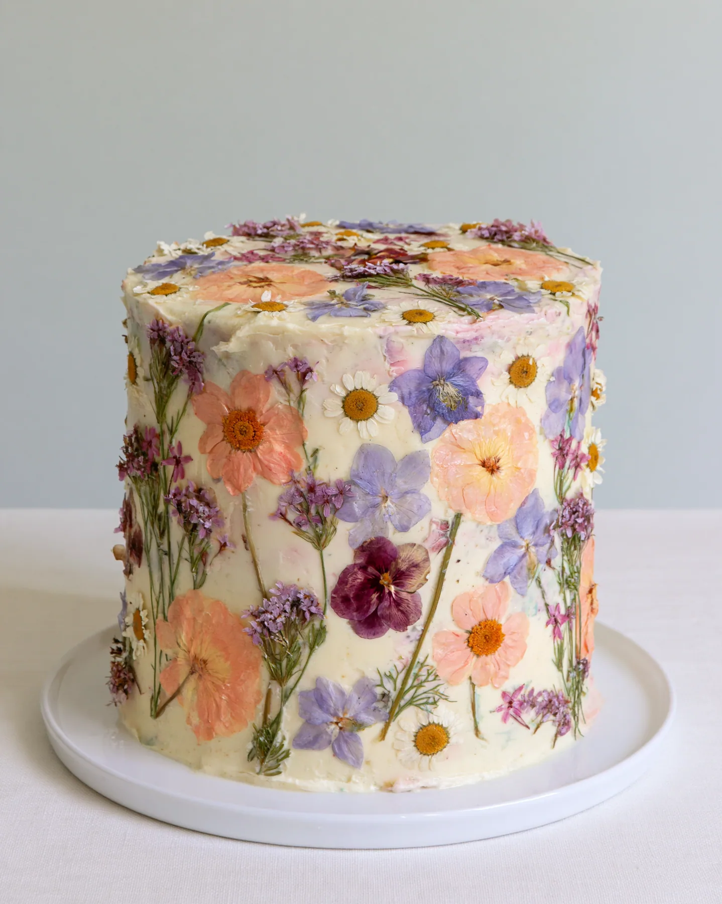 a pastel buttercream cake decorated with pressed flowers, studio light, no text, no letters, no logos