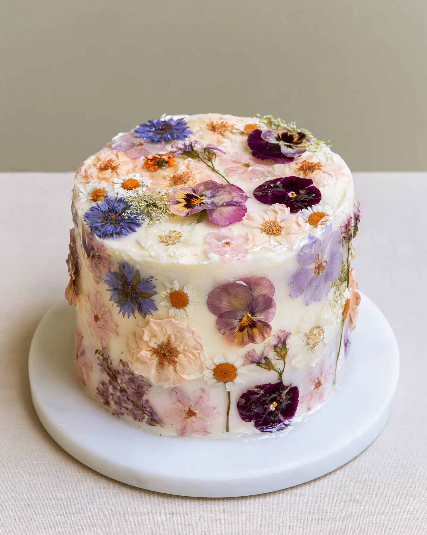 a pastel buttercream cake decorated with pressed flowers, studio light, no text, no letters, no logos