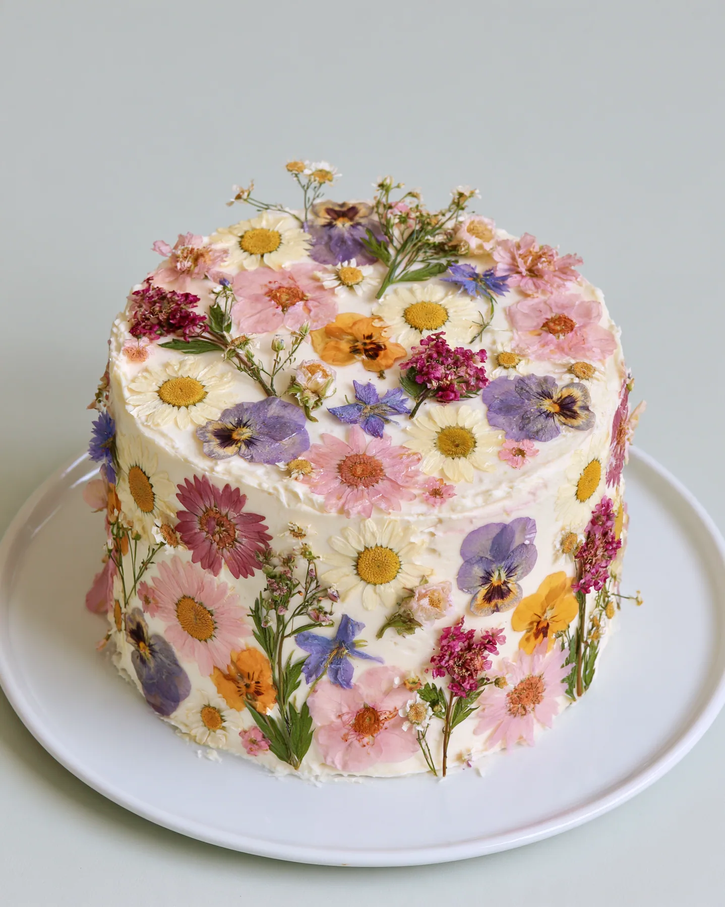 a pastel buttercream cake decorated with pressed flowers, studio light, no text, no letters, no logos