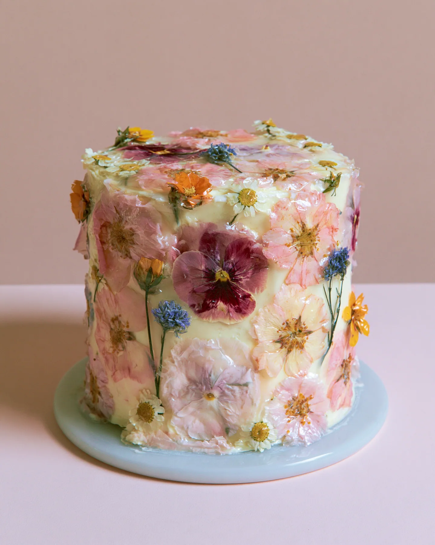 a pastel buttercream cake decorated with pressed flowers, studio light, no text, no letters, no logos