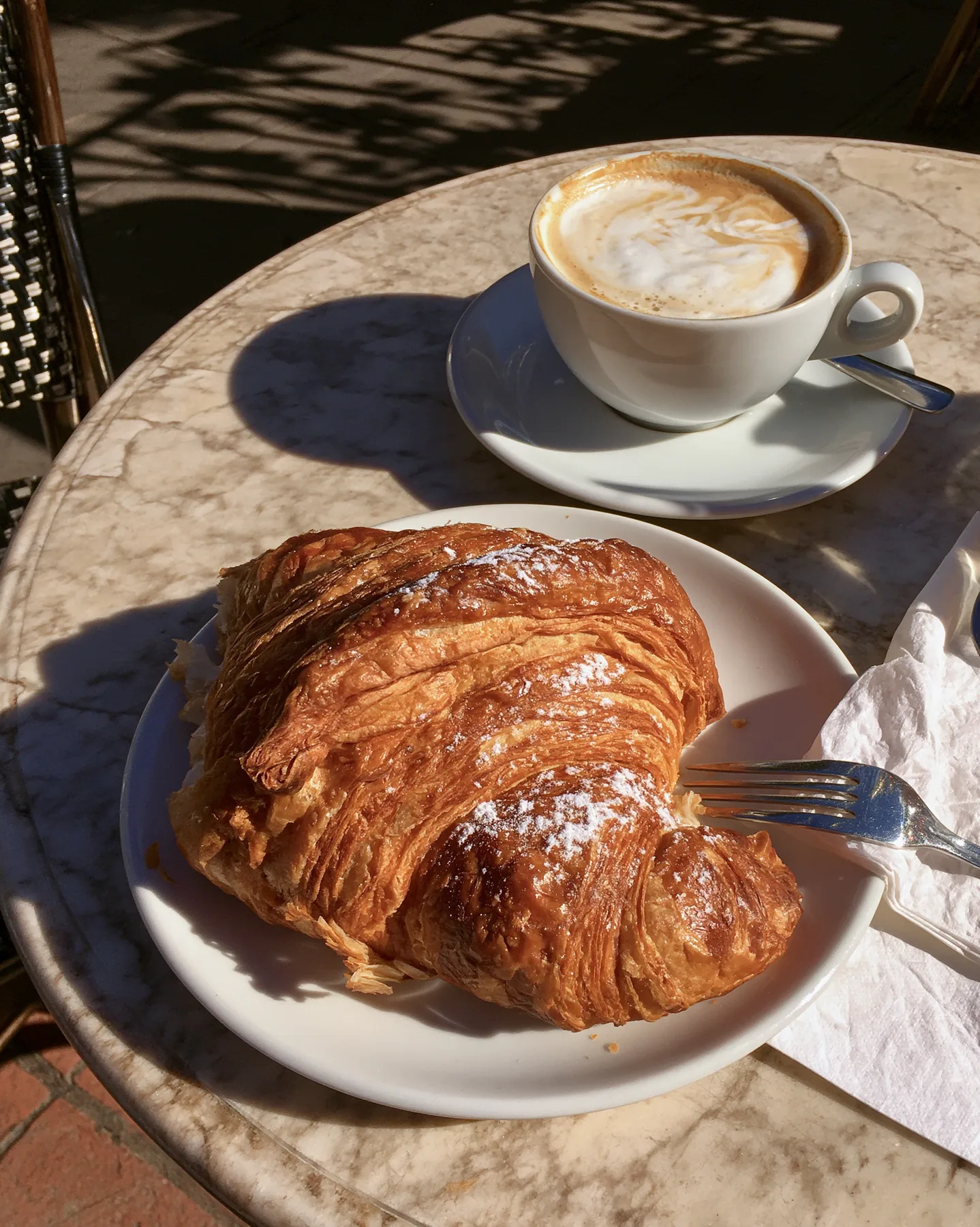 a flaky croissant on a marble cafe table with a cappuccino, morning light, no text, no letters, no logos