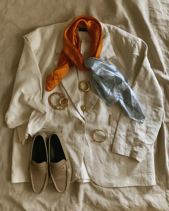 a fashion flat lay of an oversized blazer, silk scarf, loafers and gold jewelry on linen, overhead, no text, no letters, no logos
