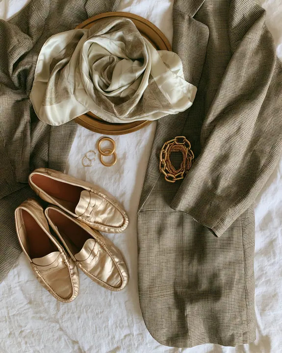 a fashion flat lay of an oversized blazer, silk scarf, loafers and gold jewelry on linen, overhead, no text, no letters, no logos