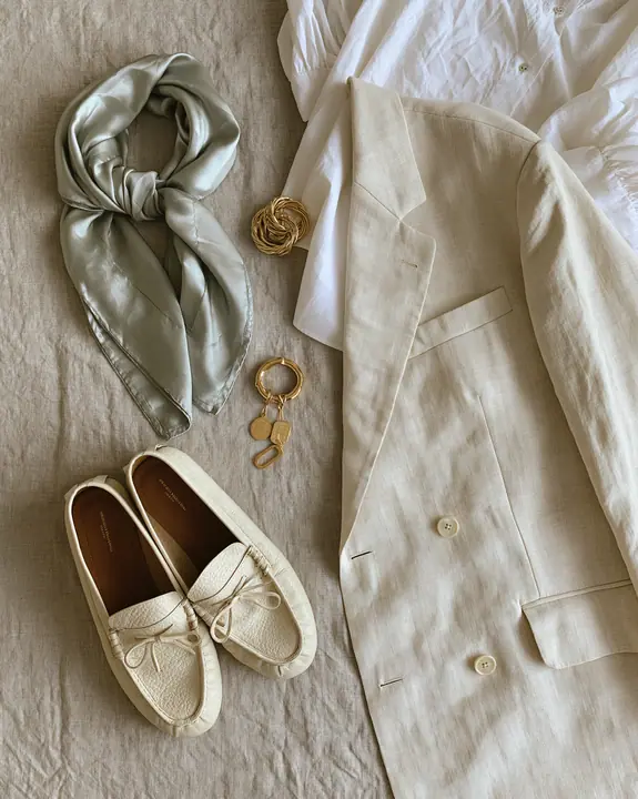 a fashion flat lay of an oversized blazer, silk scarf, loafers and gold jewelry on linen, overhead, no text, no letters, no logos