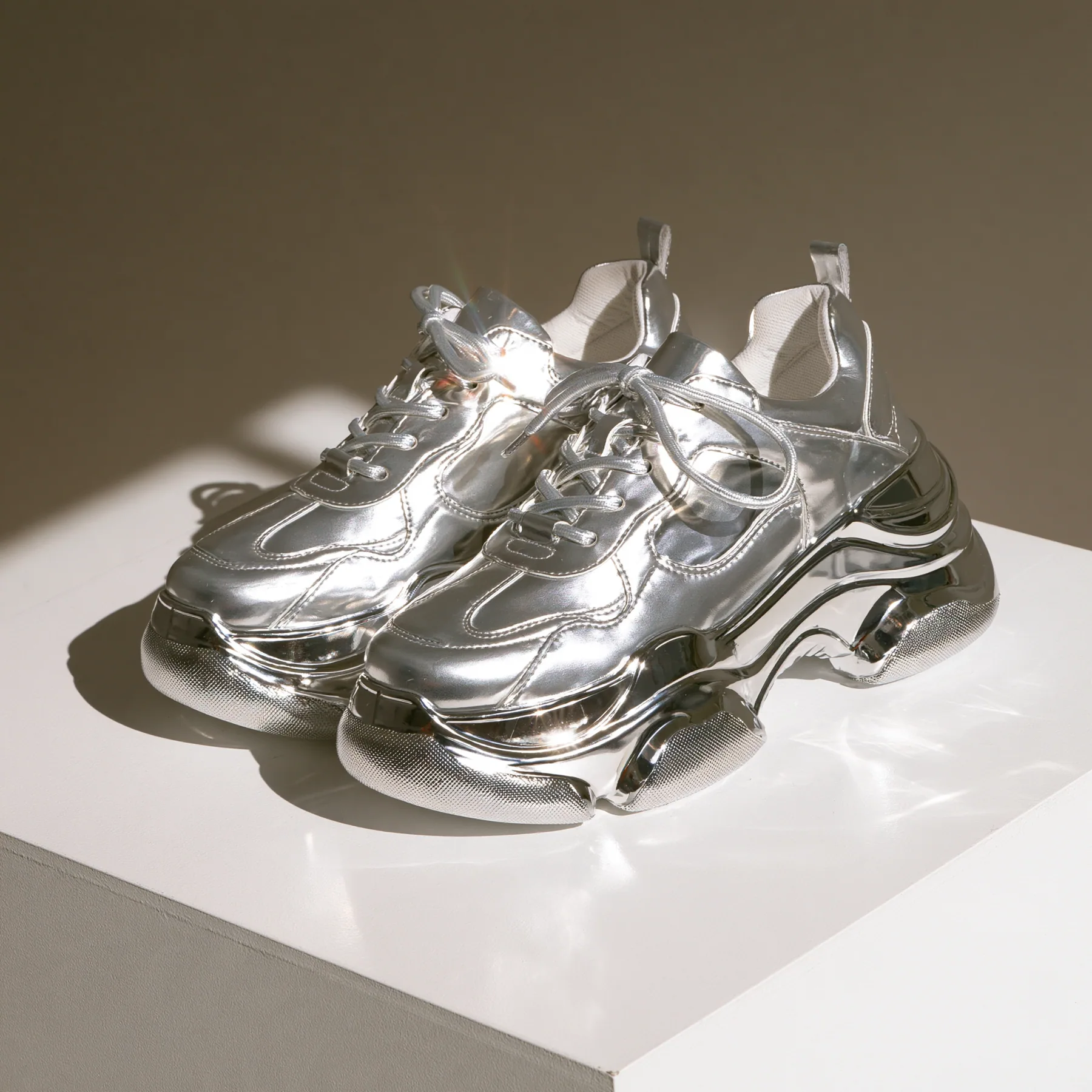 chunky silver sneakers on a white plinth, product photograph, soft shadow, no text, no letters, no logos