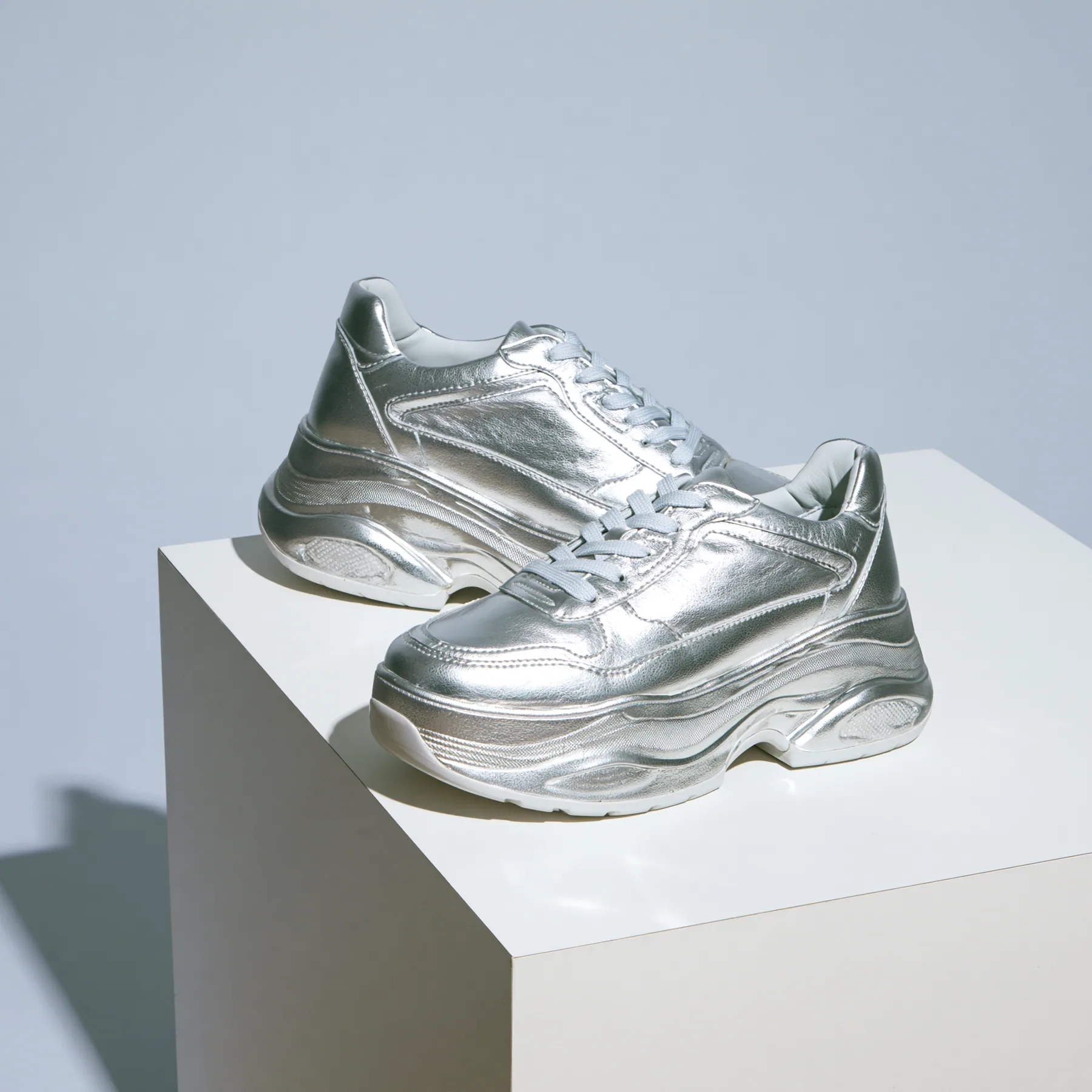 chunky silver sneakers on a white plinth, product photograph, soft shadow, no text, no letters, no logos