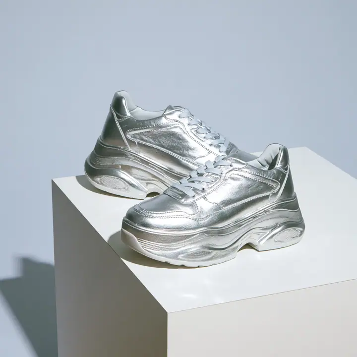chunky silver sneakers on a white plinth, product photograph, soft shadow, no text, no letters, no logos