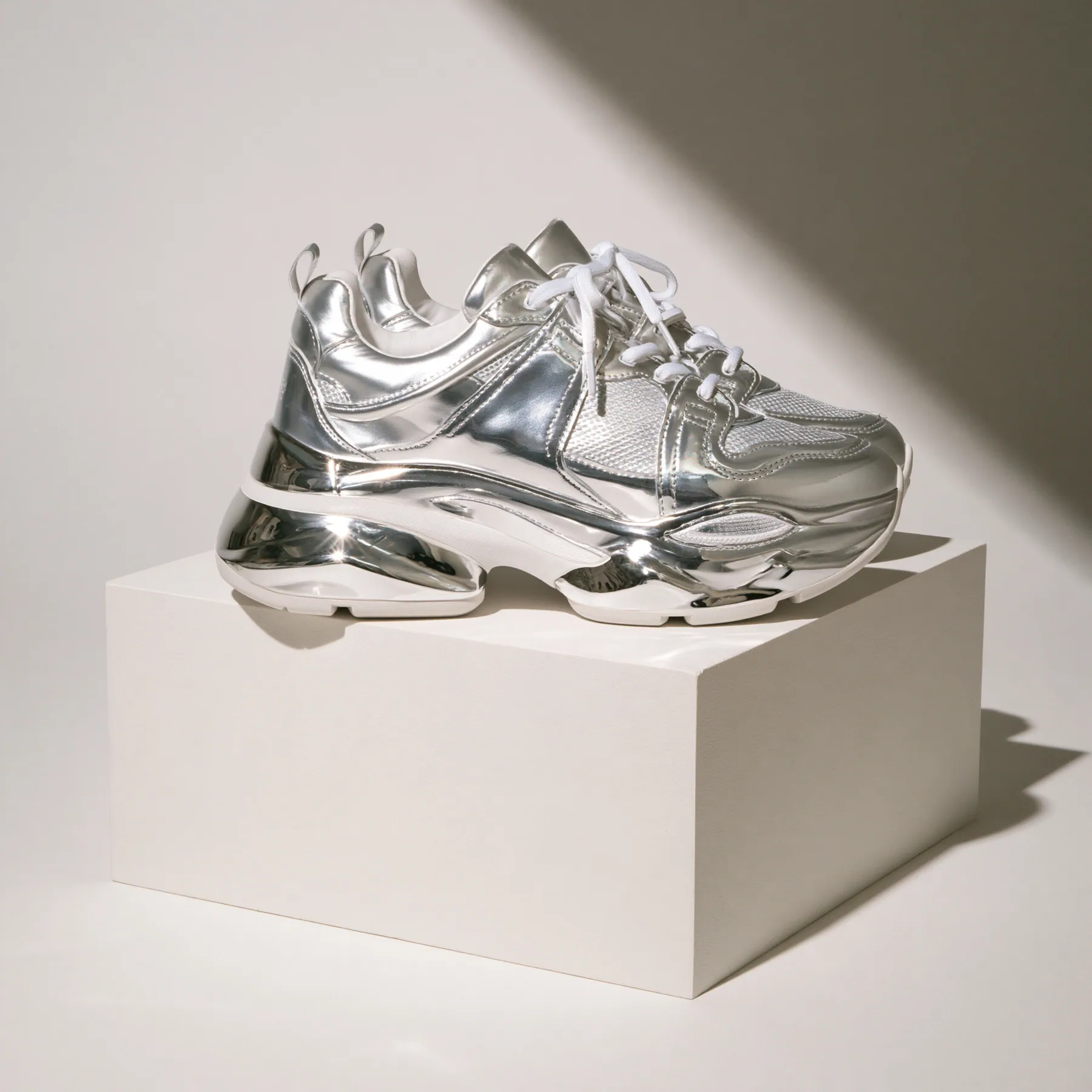 chunky silver sneakers on a white plinth, product photograph, soft shadow, no text, no letters, no logos