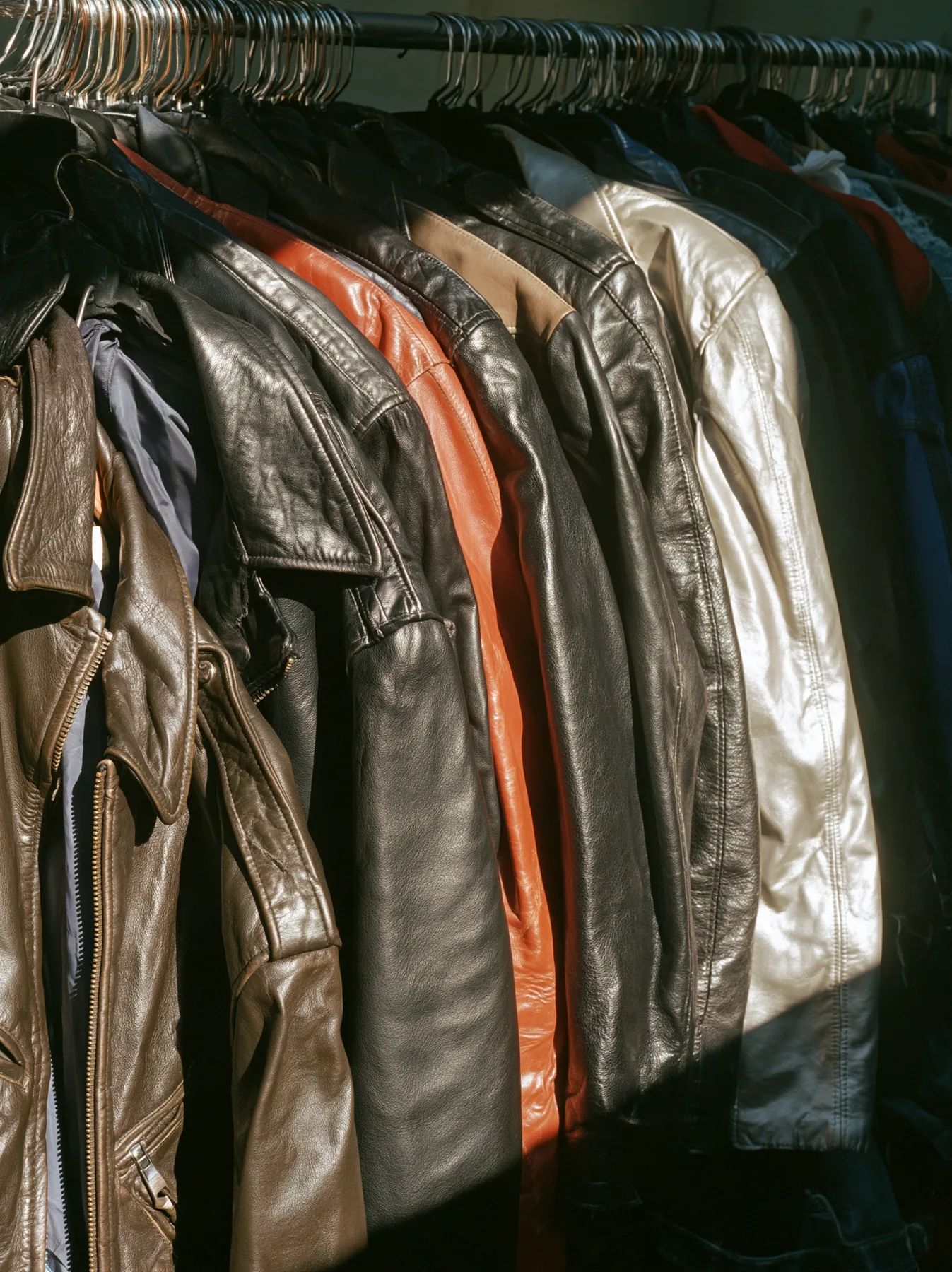 a rack of vintage leather jackets in a sunlit thrift shop, no text, no letters, no logos