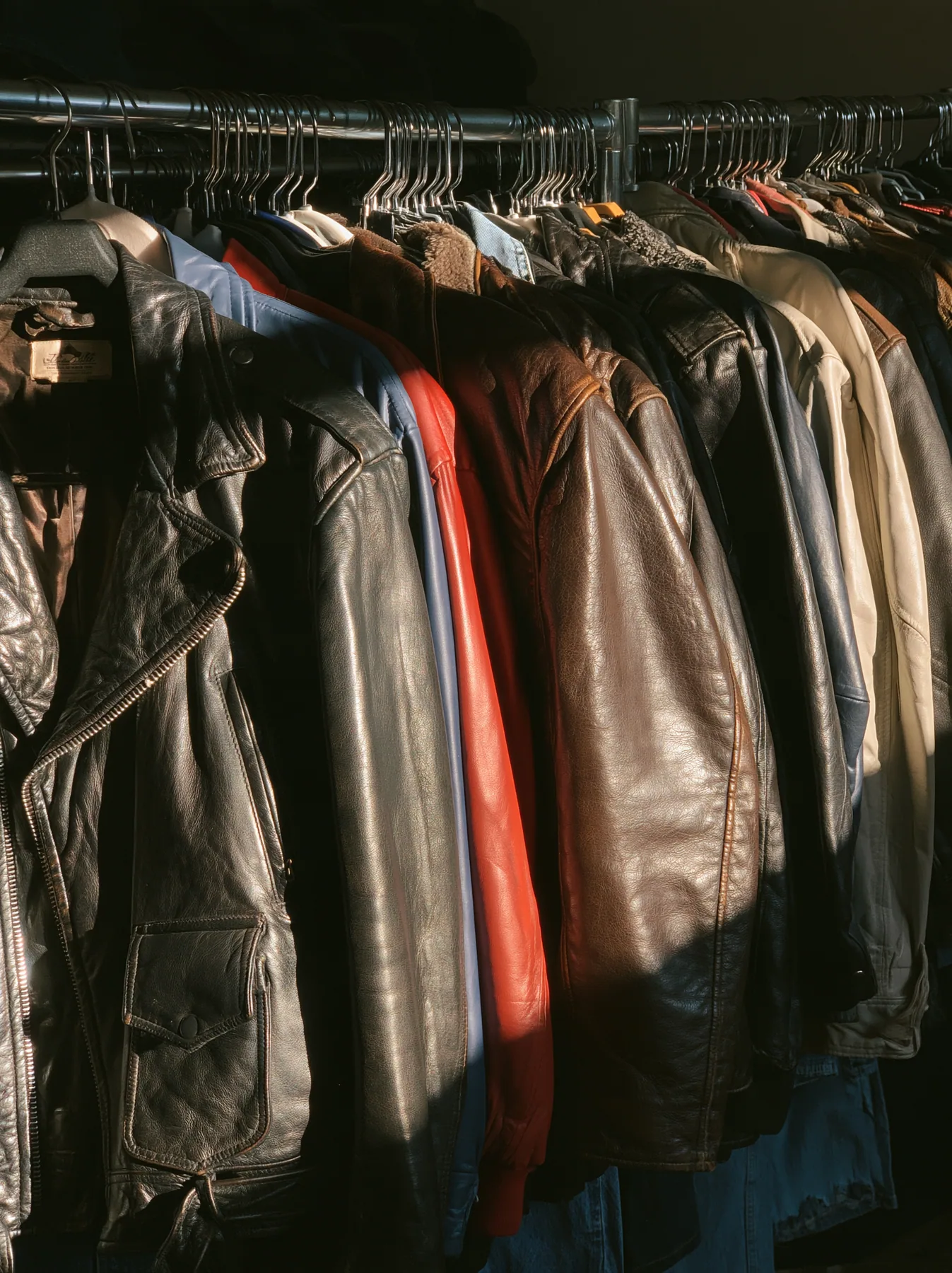 a rack of vintage leather jackets in a sunlit thrift shop, no text, no letters, no logos