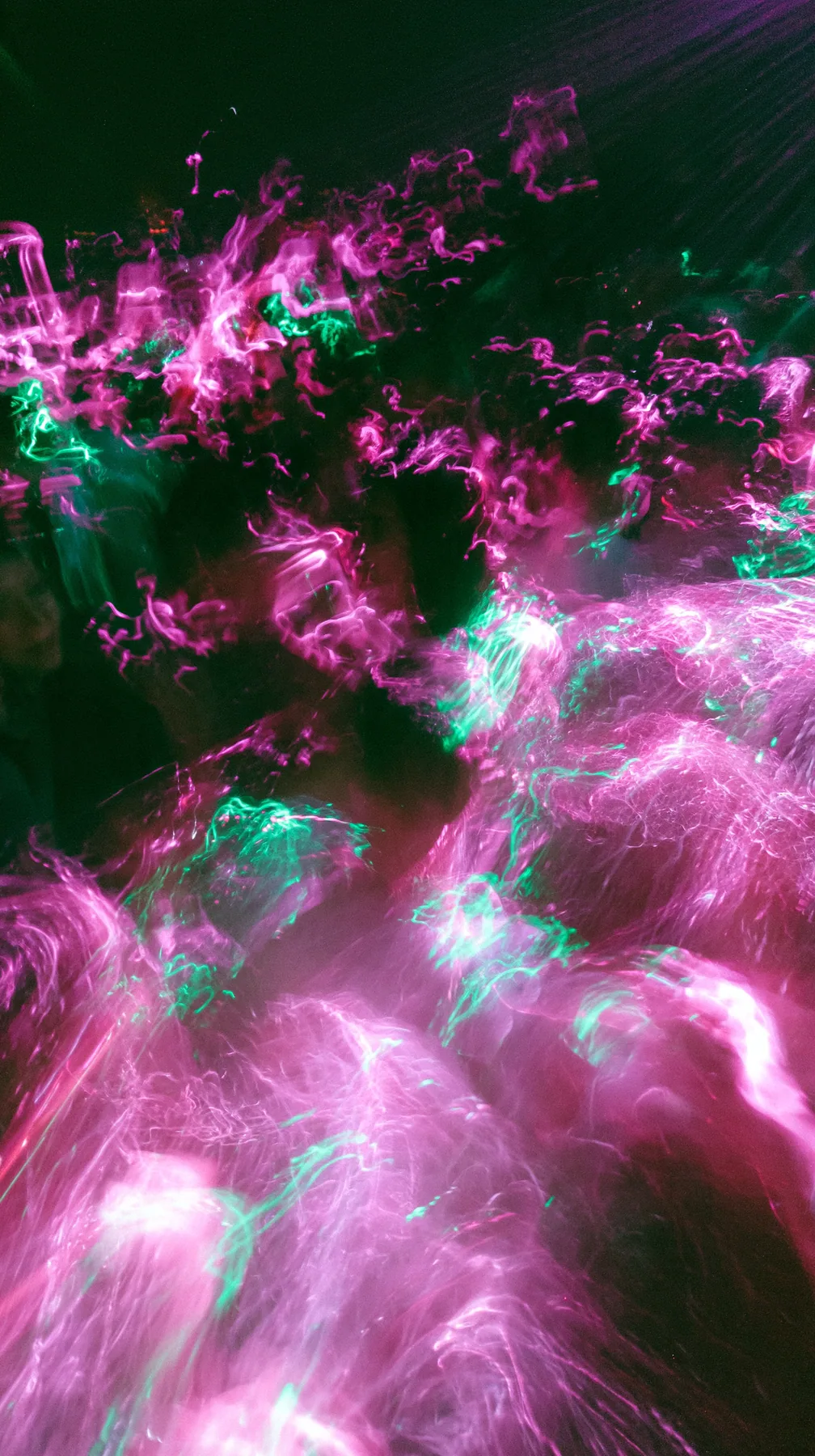 a crowded-looking dance floor reduced to long-exposure light trails of magenta and green, no faces, no text, no letters, no logos