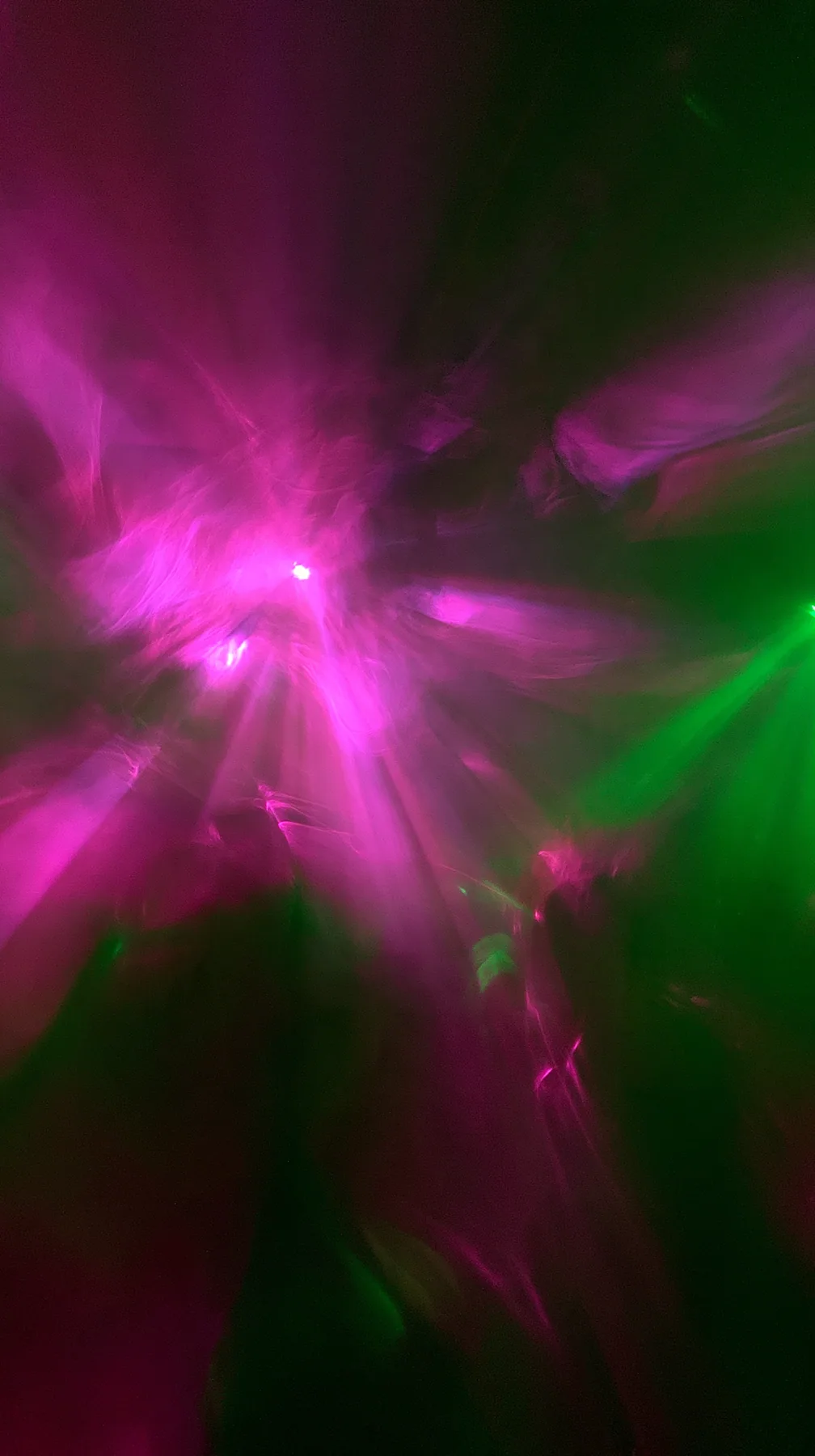 a crowded-looking dance floor reduced to long-exposure light trails of magenta and green, no faces, no text, no letters, no logos