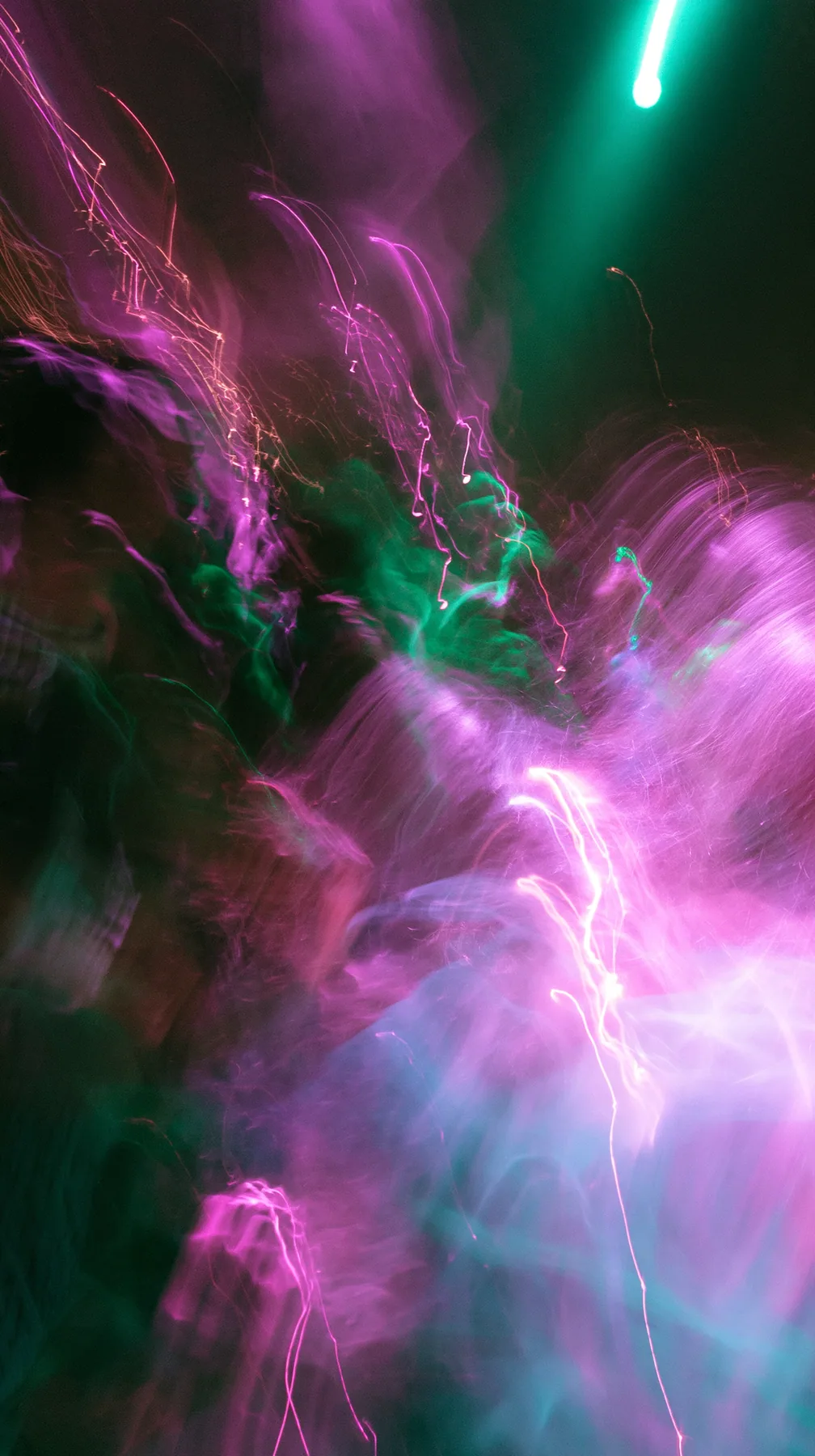 a crowded-looking dance floor reduced to long-exposure light trails of magenta and green, no faces, no text, no letters, no logos