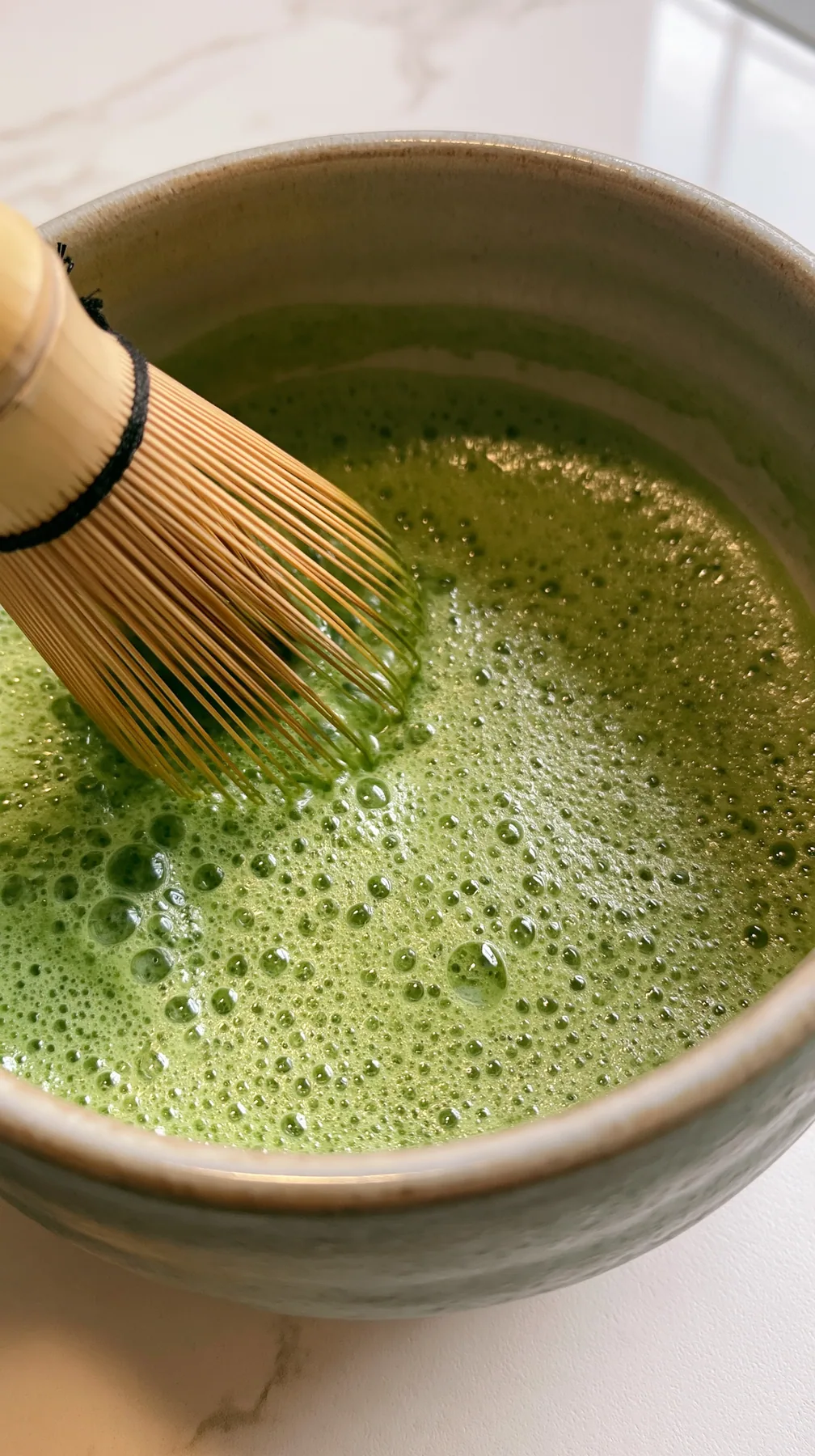 matcha being whisked in a ceramic bowl, bright green foam, overhead, no text, no letters, no logos